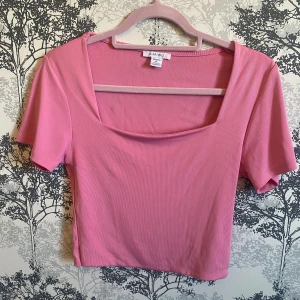 Rosa ribbad topp från Amisu - Säljer en söt rosa ribbad topp från Amisu. Den har en fyrkantig halsringning och korta ärmar, perfekt för en avslappnad stil. Toppen är i ett mjukt och stretchigt material som ger en bekväm passform. Perfekt för vår och sommar! Använt några gånger.