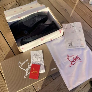 Mörkblåa sneakers från Christian Louboutin - Snygga mörkblåa sneakers från Christian Louboutin med den ikoniska röda sulan. Skorna har en stilren design med snörning och är tillverkade i mocka. Perfekta för den som vill ha en touch av lyx i vardagen.