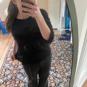 Svart fluffig tröja - Säljer en svart fluffig tröja med trekvartsärm. Tröjan har en unik textur som ger ett trendigt och mysigt intryck. Perfekt för att lägga till lite stil till din garderob. Passar bra till både jeans och kjol.