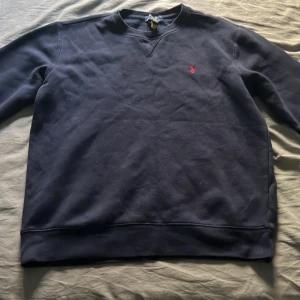 Ralph lauren tröja  - Säljer en stilren mörkblå tröja från Polo Ralph Lauren med en liten röd logga på bröstet. Tröjan har långa ärmar och en klassisk rund halsringning. Perfekt för en avslappnad och snygg look.(Det är XL i junior storlekar men passar S i herr) om ni har några frågor är det bara att skriva till mig -MVH Marko