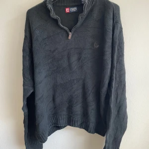 Mörkgrå stickad tröja från Chaps - Säljer en mörkgrå stickad tröja från Chaps med dragkedja vid halsen. Tröjan har långa ärmar och ribbade muddar vid ärmslut och nederkant. Perfekt för kyliga dagar.