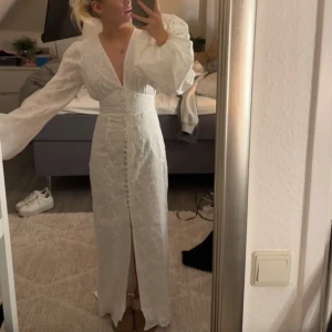 Adoore klänning - vit långklänning med v-ringning och långa ärmar. Klänningen har knappar framtill och en subtil slits. Aldrig använd. 
