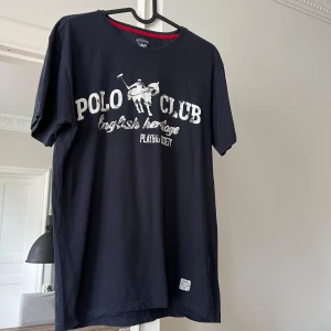Mörkblå t-shirt från Vinson Polo Club - Snygg mörkblå t-shirt från Vinson Polo Club med ett stort tryck på framsidan. T-shirten har en klassisk rund hals och korta ärmar. Säljer för endast 60kr!!