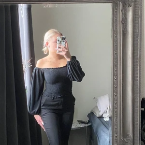 Svart offshoulder topp - Snygg svart offshoulder topp med smockad design och långa puffärmar. Perfekt för en stilren look.