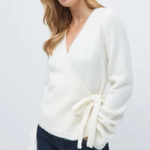 Vit kofta - Säljer en beige/vit kofta med knytband i midjan. Koftan har en v-ringad design och långa ärmar, . Den är mjuk och bekväm, snygg för både vardag och speciella tillfällen. Kan stylas enkelt med andra plagg💕