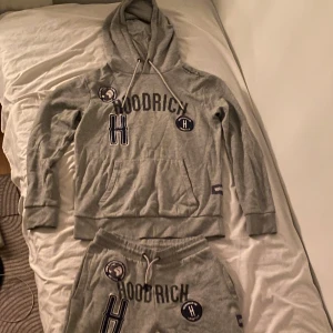 Grå hoodie och byxor från Hoodrich - Säljer en grå hoodie och matchande byxor från Hoodrich. Hoodien har en stor logotyp på bröstet och en praktisk ficka framtill. Byxorna har samma logotyp och justerbar dragsko i midjan. Perfekt för en avslappnad stil.(priset kan diskuteras)