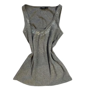 Glittrigt paljett linne från Lindex  - Snygg grå ärmlös topp från Lindex med glittrande detaljer vid halsringningen. Perfekt för att lägga till lite bling till din outfit. Använt skick men fortfarande fin. 