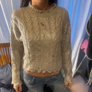 Beige stickad tröja med guld detaljer  - Säljer en beige stickad tröja med guld detaljer. Tröjan har ett flätmönster och är croppad med långa ärmar. Perfekt för att lysa upp din garderob! ✨