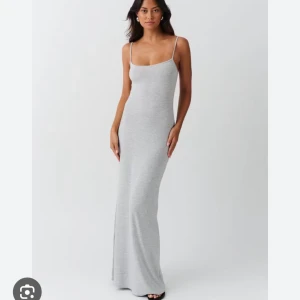 Grå långklänning med smala axelband - Snygg och stilren grå långklänning med smala axelband. Perfekt för en minimalistisk look. Klänningen har en tight passform som framhäver figuren.