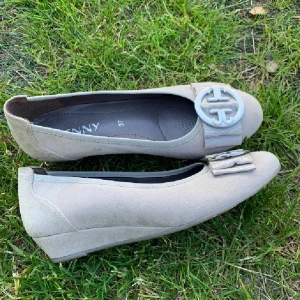 Beige ballerinaskor från Jenny - Snygga beige ballerinaskor från Jenny med en dekorativ detalj framtill. Skorna har en låg klack och är perfekta för en stilren look. De är tillverkade i ett mjukt material som ger en bekväm passform.