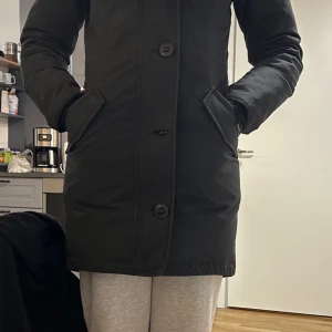 Svart parkajacka från Canada Goose - Säljer en svart parkajacka från Canada Goose med pälsdetaljer på huvan. Jackan har långa ärmar och knäppning framtill. Perfekt för kalla vinterdagar. Jacka är använd max 5-6 gånger. Köpt i thernlunds. Pris kan diskuteras vid snabb affär.