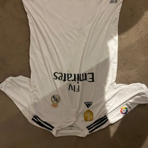 Vit Real Madrid fotbollströja - Säljer nu denna feta real tröjan från 2018 med Ramos på ryggen, tröjan är köpt i Madrid men väldigt sparsamt använt då den varit i en samling.  Tröjan är storlek XL men skulle säga mer L, kom med bud då priset ej är hugget i sten  
