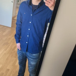 Blå skjorta från Morris - Snygg blå skjorta från Morris med klassisk krage och knappar framtill. Skjortan har långa ärmar och en liten broderad logga på bröstet. Perfekt för en stilren look.