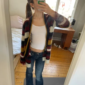 Flerfärgad stickad kofta från Boomerang - Säljer en mysig flerfärgad stickad kofta från Boomerang. Koftan har ett randigt mönster i rött, blått, vitt och gult. Den är tillverkad i en blandning av nylon, kidmohair och ull, vilket gör den både varm och bekväm. Perfekt för kyliga dagar! Passar mig som är xs men passar också s och xxs Den är perfekt i armarna för mig som är 160 cm💕💕💕🫶🏻