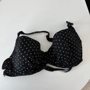 Svart prickig bikiniöverdel från Bodyzone - Snygg svart bikiniöverdel med vita prickar från Bodyzone. Den har justerbara axelband och en praktisk knäppning i ryggen. Använd som ni ser på bilderna 