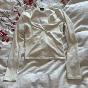 Vit långärmad topp från Gina tricot  - Säljer en stilren vit långärmad topp från Gina tricot. Toppen har en elegant v-ringning och är tillverkad i ett mjukt material som ger en skön passform. Perfekt för både vardag och festliga tillfällen. Passar bra till jeans eller kjol!