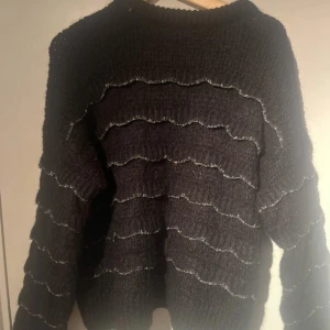 Svart stickad tröja med vågigt mönster - Säljer en svart stickad tröja med ett unikt vågigt mönster. Tröjan har långa ärmar och en rund halsringning. Perfekt för kyligare dagar.