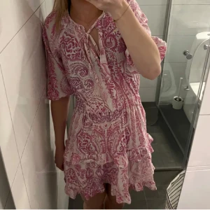 Rosa mönstrad klänning - Säljer en söt rosa klänning med ett vackert mönster och volangdetaljer. Klänningen har trekvartsärmar och en knytning framtill. Perfekt för sommarens alla tillfällen! Köpte på Plick för någon månad sen men säljer pågrund av att den tyvärr va för liten❤️❤️