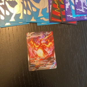 Charizard VMAX Pokémonkort - Säljer ett Charizard VMAX Pokémonkort med en imponerande design i eldiga färger. Kortet har en styrka på 330 och är en del av VMAX-serien. Perfekt för samlare eller spelare som vill förstärka sin kortlek med en kraftfull eld-Pokémon.