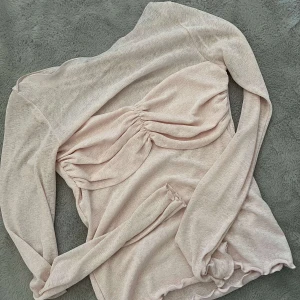 Ljusrosa topp från Gina Tricot - Säljer en ljusrosa topp från Gina Tricot med långärmad design och snygg rynkdetalj framtill. Perfekt för en stilren look.
