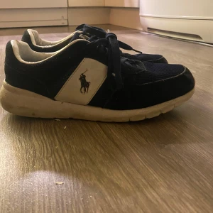 Polo Ralph Lauren sneakers - Snygga mörkblå sneakers från Polo Ralph Lauren med vit sula och logotyp på sidan. Skorna är i jättefint skick. Lite slitna på själva insidan men allt annat är i jättefint skick😊