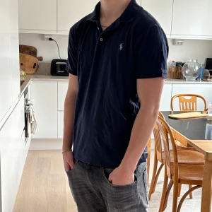 Mörkblå pikétröja från Ralph Lauren - Säljer en stilren mörkblå pikétröja från Ralph Lauren med klassisk krage och knappdetaljer. Perfekt för en avslappnad men ändå snygg look.