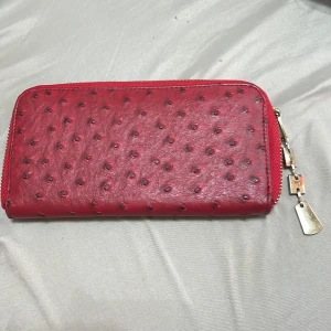 Röd plånbok med dragkedja - Snygg röd plånbok med dragkedja och ett unikt mönster som påminner om strutsläder. Den har en guldfärgad dragkedja med en dekorativ kedja som detalj. Perfekt för att hålla ordning på kort och kontanter.❤️