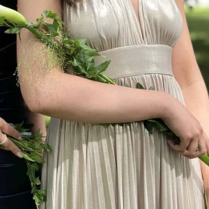 Champagnefärgad långklänning - Elegant champagnefärgad långklänning med djup v-ringning och öppen rygg. Klänningen har ett brett band i midjan och ett vackert fall som ger en lyxig känsla. Perfekt för speciella tillfällen.