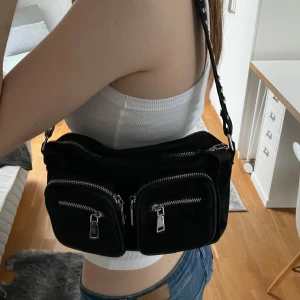 Svart axelväska med nitar - Säljer denna snygga svarta axelväskan från Noella, äkta! Har flera dragkedjefickor framtill och nitar på axelremmen. Är verkligen en så snygg väska, använd men ändå i fint skick! Mellanstor modell, nypris 799. Hör av er om frågor💕