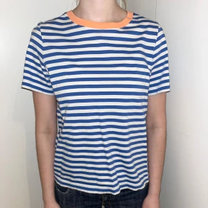 Randig t-shirt från COS - Säljer en snygg randig t-shirt från COS i blått och vitt med en cool orange krage. Perfekt för en avslappnad stil. Passar bra till jeans eller shorts!