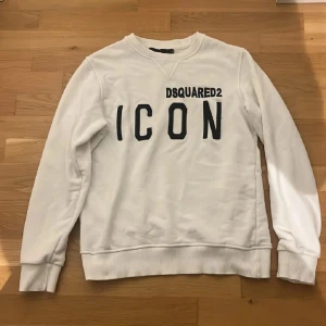 Vit sweatshirt från Dsquared2 - Säljer en stilren vit sweatshirt från Dsquared2 med texten 'ICON' i svart på framsidan. Tröjan har långa ärmar och ribbade muddar vid ärmslut och nederkant. Perfekt för en casual look!