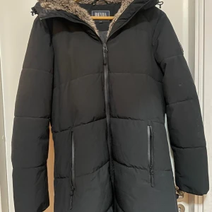 Svart dunjacka från Didriksons - Säljer en svart dunjacka från Didriksons med huva och dragkedja framtill. Jackan har långa ärmar och två praktiska fickor med dragkedja. Perfekt för kalla dagar!