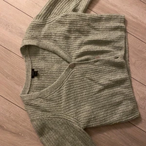 Grön stickad kofta från Lindex - Mysig grön stickad kofta från Lindex med knappar framtill. trekvartärm, Perfekt för kyliga dagar och ger en avslappnad look. Koftan har en mjuk textur och en klassisk design.