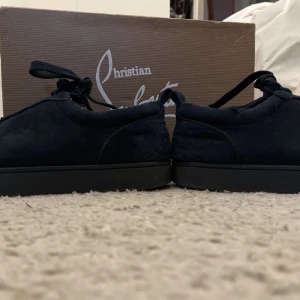 Svarta sneakers från Christian Louboutin - Snygga svarta sneakers från Christian Louboutin med klassisk röd sula. Skorna har snörning och är tillverkade i mocka, vilket ger en lyxig känsla. Perfekta för den som vill ha stilrena och exklusiva skor.