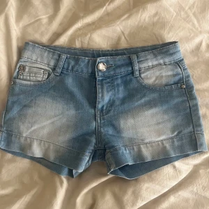 Blå jeansshorts - Snygga blå jeansshorts med klassisk femficksdesign och knappstängning. De har en lätt tvättad look och dragkedjedetaljer på bakfickorna för en extra touch. Perfekta för en avslappnad stil.