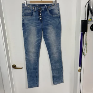 Blå jeans med knappar - Snygga blå jeans med 5 knappar fram och fem fickor. De har en tight passform och är perfekta för en avslappnad stil. Jeansen har en klassisk blå tvätt och är tillverkade i ett bekvämt denimtyg.