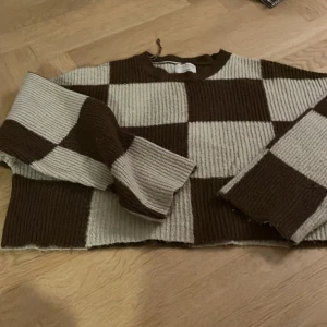 Brun och beige rutig tröja från Pull&Bear - Säljer en cool brun och beige rutig tröja från Pull&Bear. Tröjan har en croppad passform och är ribbad vilket ger den en unik look. Perfekt för att sticka ut i mängden!