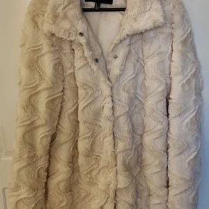 Beige pälsjacka från Veromoda - Säljer en supermjuk och fluffig beige pälsjacka från Veromoda. Jackan har en snygg struktur med långa ärmar och knappar framtill. Perfekt för att hålla sig varm och stilren under kyliga dagar.