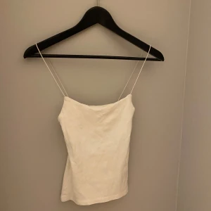 Vitt linne från Zara - Säljer ett vit linne från Zara med tunna axelband. Perfekt för varma sommardagar eller som ett basplagg i garderoben. Enkel och elegant design som passar till det mesta.