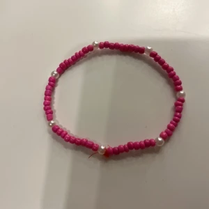 Rosa pärlarmband - Charmigt armband med rosa pärlor och vita detaljer. Perfekt för att lägga till en färgklick till din outfit.