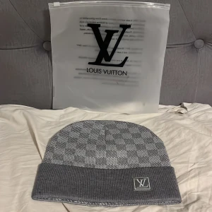 Ljus grå rutig mössa från Luviton - Snygg grå mössa från Luviton med ett rutigt  mönster och uppvikt kant. Mössan har en broderad Luviton-logga framtill och är otroligt skön och stilig att ha på sig!! Helt oanvänd oxh fräsch. Levereras med förpackning också. PRISET KAN DISKUTERAS.