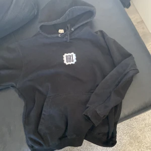 Svart hoodie från ODZ - Säljer en svart hoodie från ODZ med en vit logga på bröstet. Den har en klassisk känguruficka och justerbar huva med dragsko. Perfekt för en avslappnad stil. Hör av dig vid intresse!