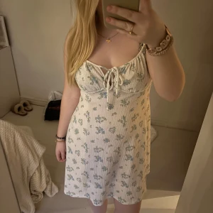 Blommig klänning med knytband - Söt blommig klänning i ljusa färger med knytband framtill. Klänningen har smala axelband och ett mjukt, ribbat material som ger en bekväm passform. 