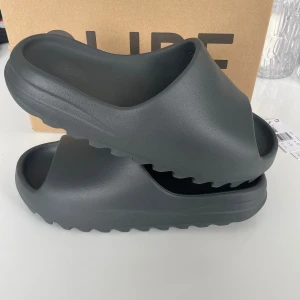 Yeezy slide dark onyx från adidas - Säljer ett par stilrena grå YZY Slide från Adidas. Dessa slides har en enkel och modern design med en bekväm passform. Perfekta för en avslappnad look. Perfekt inför sommaren, utomhus på gymmet och promenader. Knappt använda och är i bra skick. Tar bud 🤩