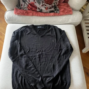 Svart tröja från Riley - Säljer en stilren svart tröja från Riley med v-ringning. Tröjan har långa ärmar och är tillverkad i ett mjukt material som passar perfekt för kyligare dagar. Perfekt för en klassisk och tidlös look.