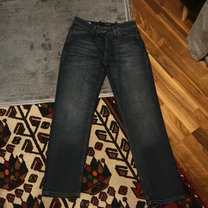 Mörkblå jeans från Jack & Jones - Snygga mörkblå jeans från Jack & Jones med en klassisk femficksdesign. De har en rak passform och är perfekta för en avslappnad stil. Jeansen har en knappgylf och är tillverkade i ett slitstarkt denimtyg.