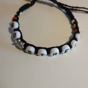 Svart armband med textpärlor - Unikt handgjort armband med texten 'NO STRESS' i vita pärlor med svarta bokstäver. Armbandet har även färgglada detaljer i rött, gult och vitt samt en liten silverfärgad dekoration. Perfekt för en avslappnad stil. Armbandet är justerbart, den minsta diametern är 6 cm 