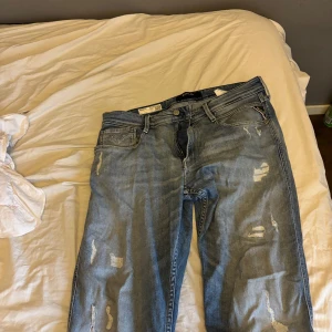 Replay anbass med slitningar - Snygga blå jeansbyxor från Replay, modell Anbass. De har en klassisk femficksdesign och slitna detaljer för en trendig look. Perfekta för en avslappnad stil.