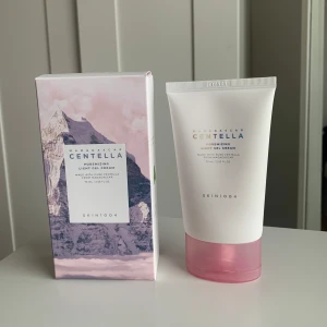 Skin1004 Madagascar Centella Light Gel Cream - Skin1004 Madagascar Centella Light Gel Cream är en återfuktande gelkräm med centella-extrakt. Den kommer i en vit tub med rosa lock och en matchande kartong med bergsmotiv. Perfekt för att ge huden en fräsch och återfuktad känsla.