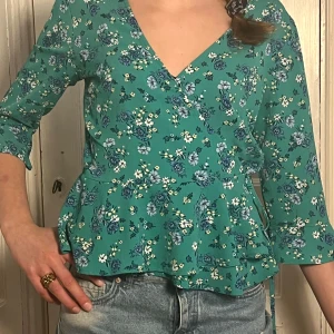 Grön blommig omlottblus💚 - Säljer en söt grön blommig omlottblus med trekvartsärmar och volangdetaljer. Storlek 40 men passar 34. Perfekt för våren och sommaren! Hör av dig vid intresse💓